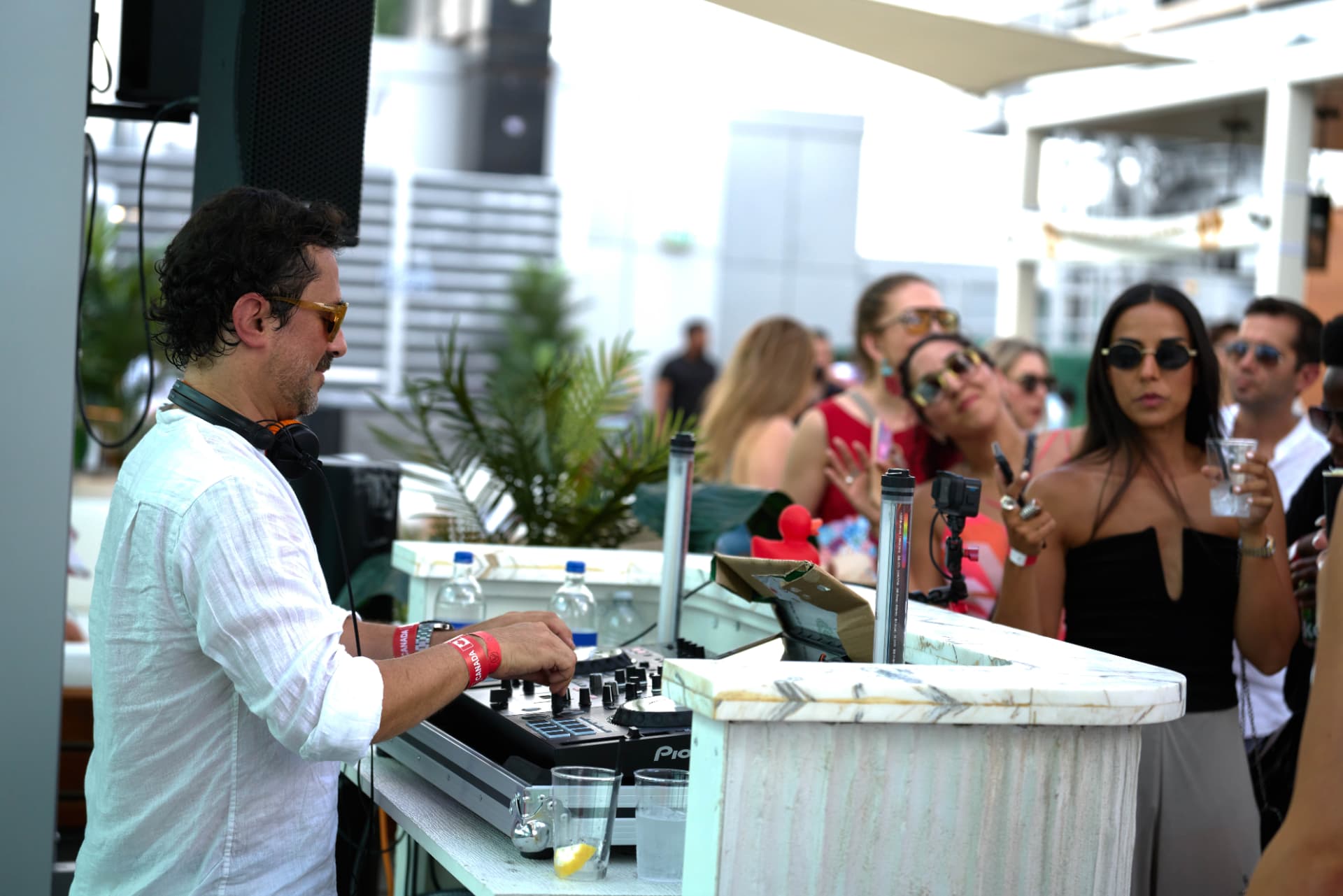 DJ playing to a sunlit rooftop crowd gathered by the marble bar