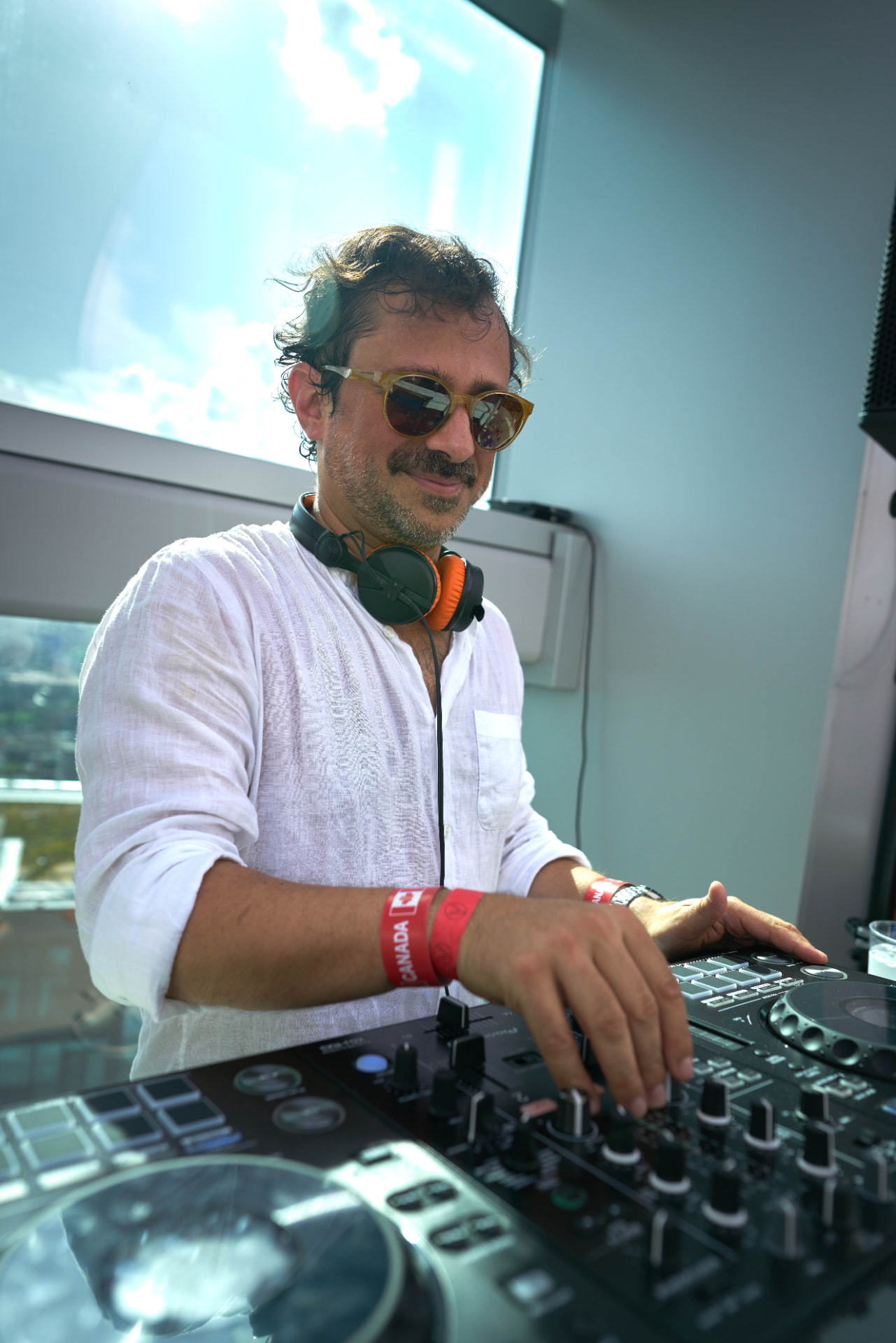 DJ in a white linen shirt mixing on the controller with the sky behind him