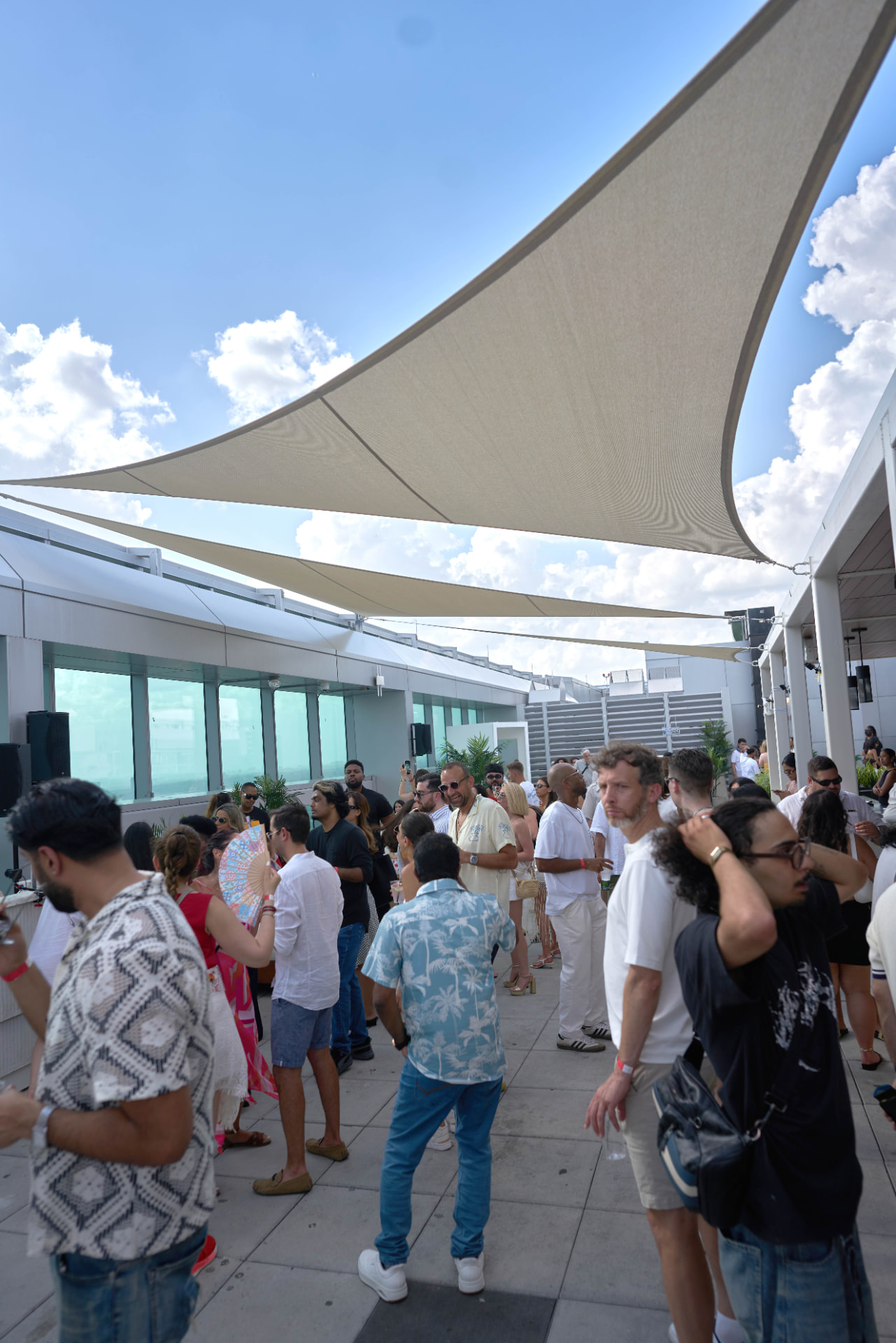 Daytime rooftop crowd gathered under shade sails at a Parkway party